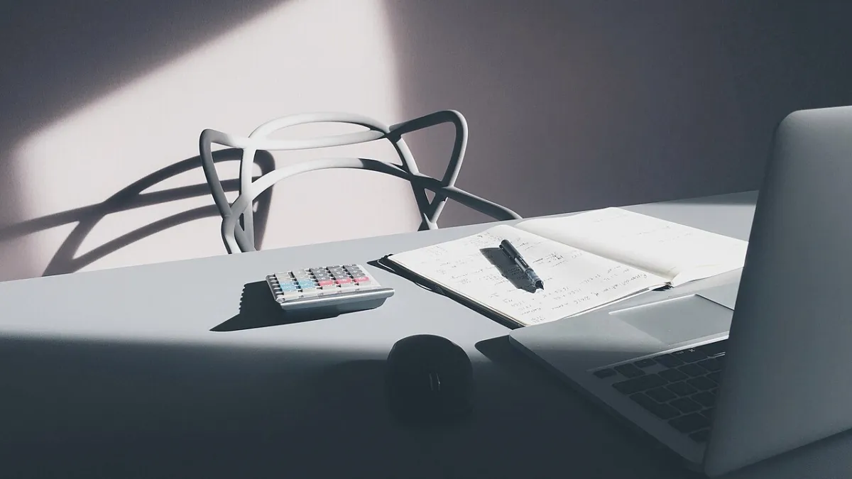 A desk with a laptop, a calculator and paperwork, used to compare AI software subscription costs