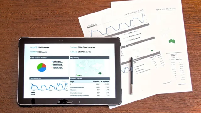 Tablet showing an analytics dashboard beside printed business reports, illustrating how NetSuite SuiteAgents monitor finance and operations workflows