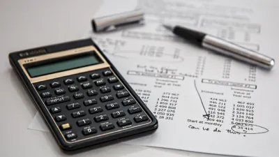 Calculator and pen resting on financial documents with calculations, representing budgeting for AI tool pricing