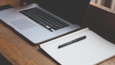 Laptop and notebook on a wooden desk, representing AI writing tools for small business marketing teams