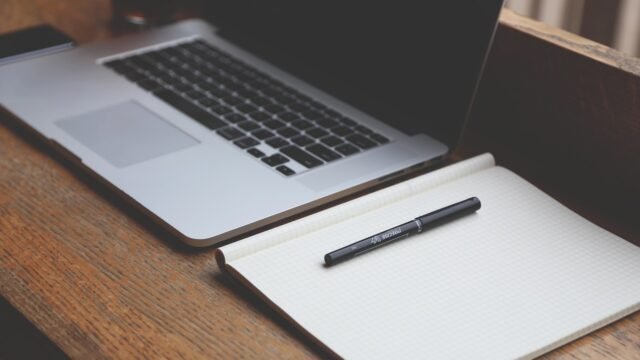 Laptop and notebook on a wooden desk, representing AI writing tools for small business marketing teams