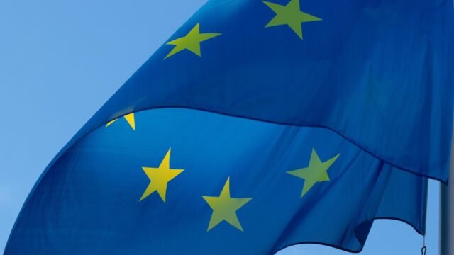 European Union flag with yellow stars on blue waving in the wind against a blue sky, representing the EU AI Act