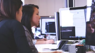 Two women collaborate at computers in a modern office, a teamwork scene illustrating Microsoft Agensh coding agents