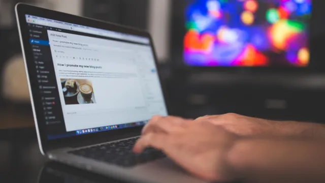 Hands typing on a laptop showing a blog post editor, representing writing AI prompt templates